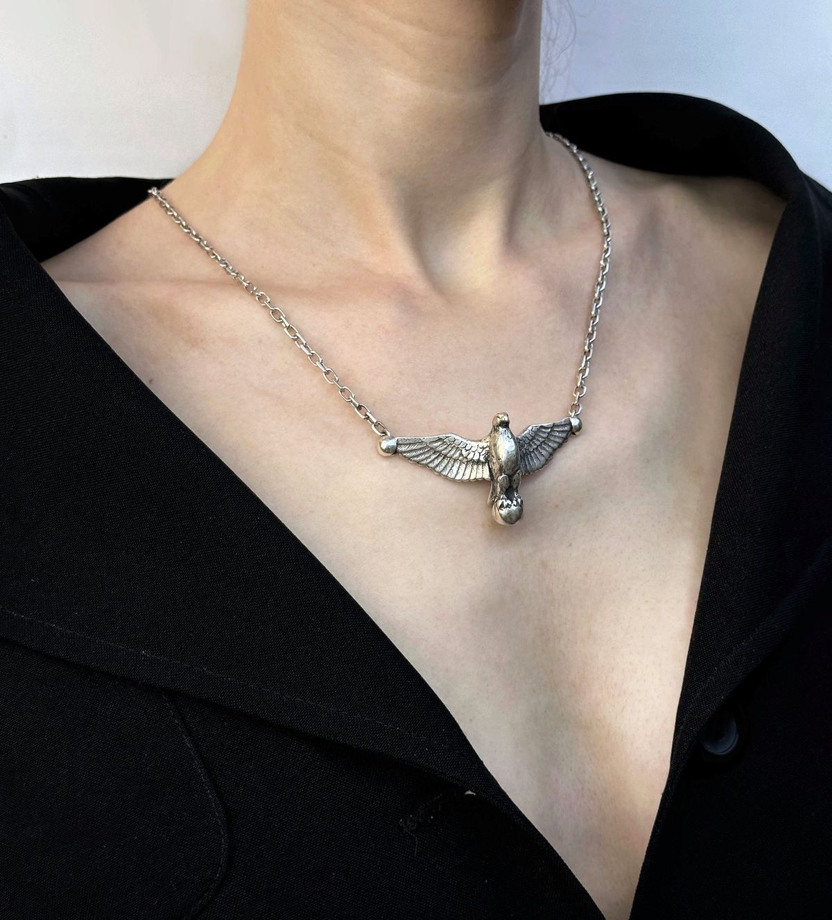 Colgante de plata en forma de águila con alas abiertas sobre una camisa negra.