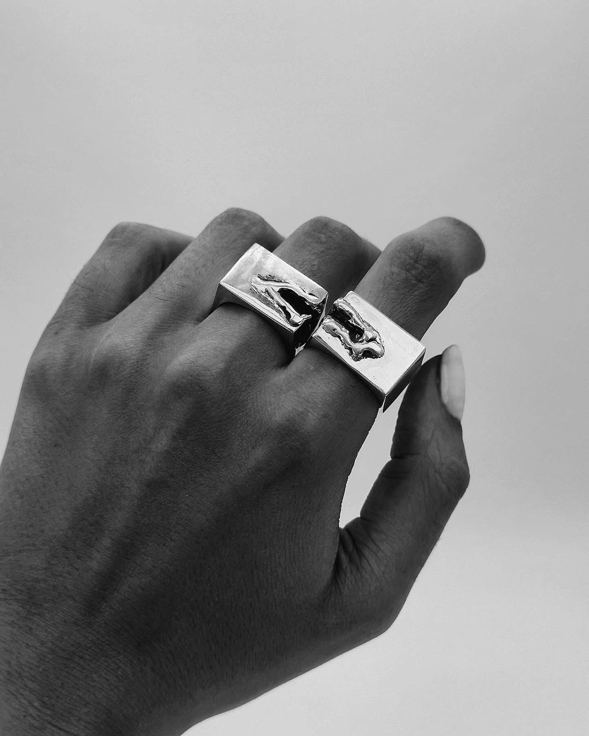 Mano en blanco y negro con dos anillos cuadrados de plata.