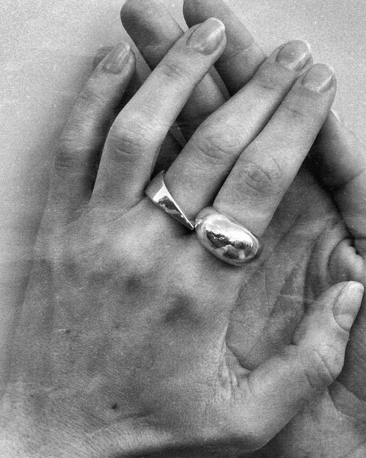Fotografía en blanco y negro de dos manos con dos anillos abombados de plata, de AGAPE.