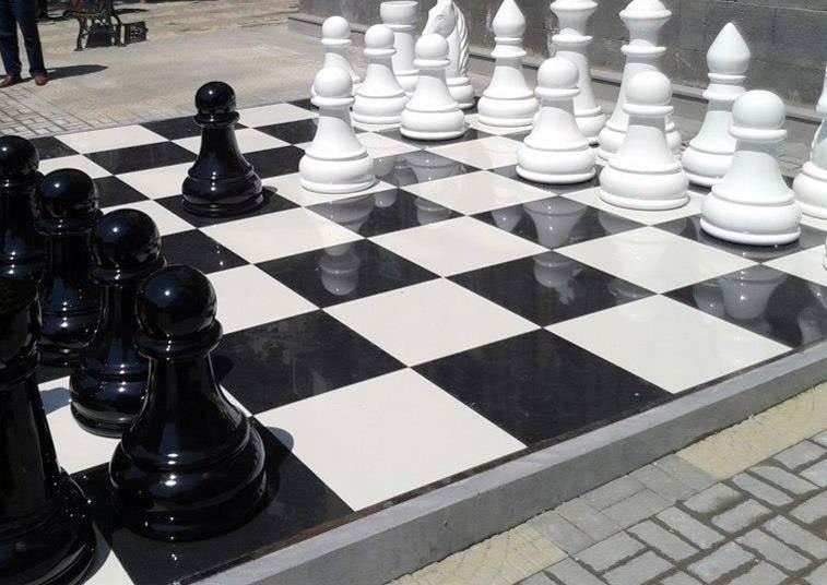 Piezas de un ajedrez gigante de fibra de vidrio, negras y blancas, sobre un tablero al aire libre en Ereván.