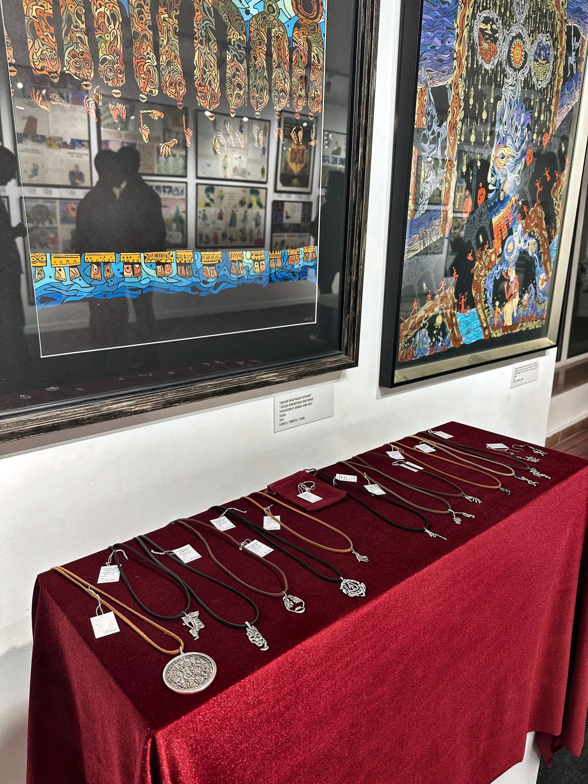 Vitrina de la exposición con colgantes sobre una mesa roja, bajo los cuadros.