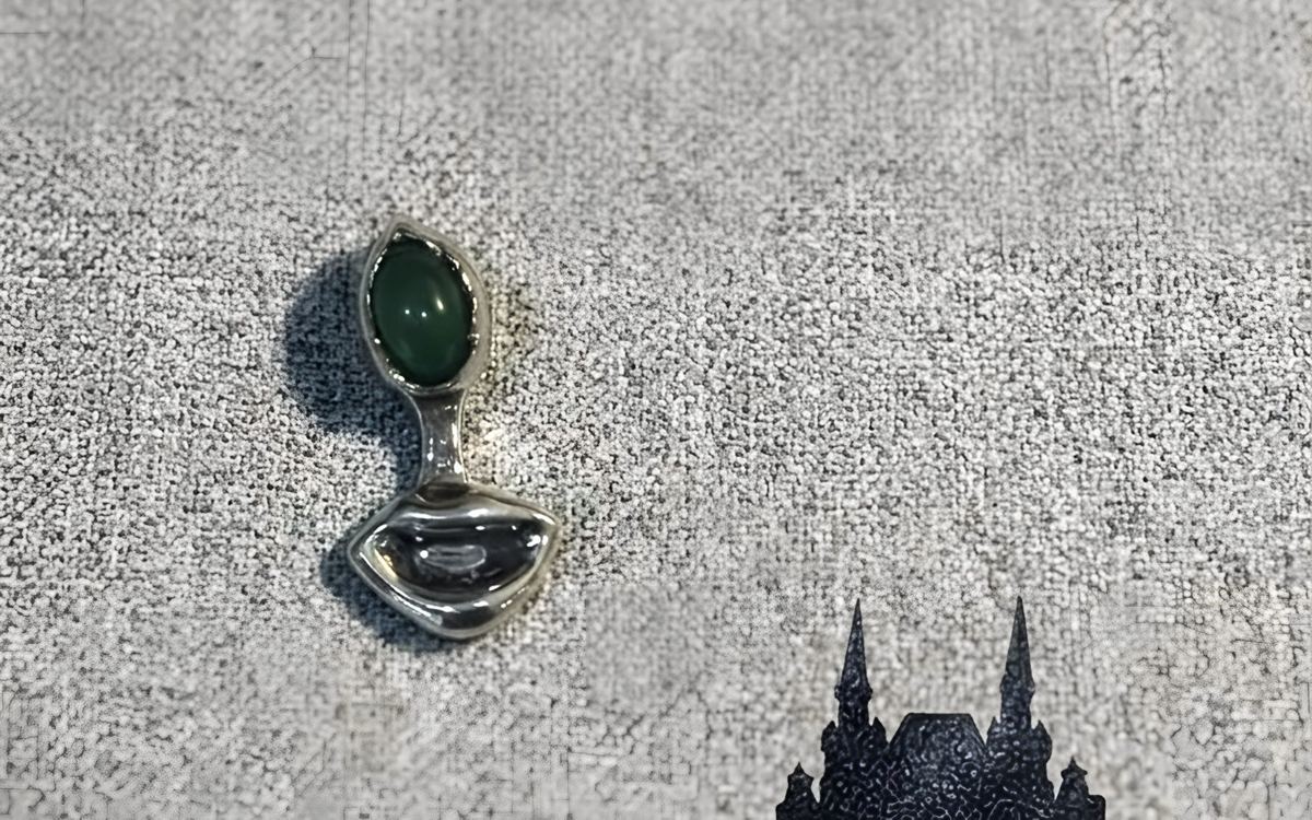 Colgante de plata con forma de labios y una nefrita verde, sobre tela gris.