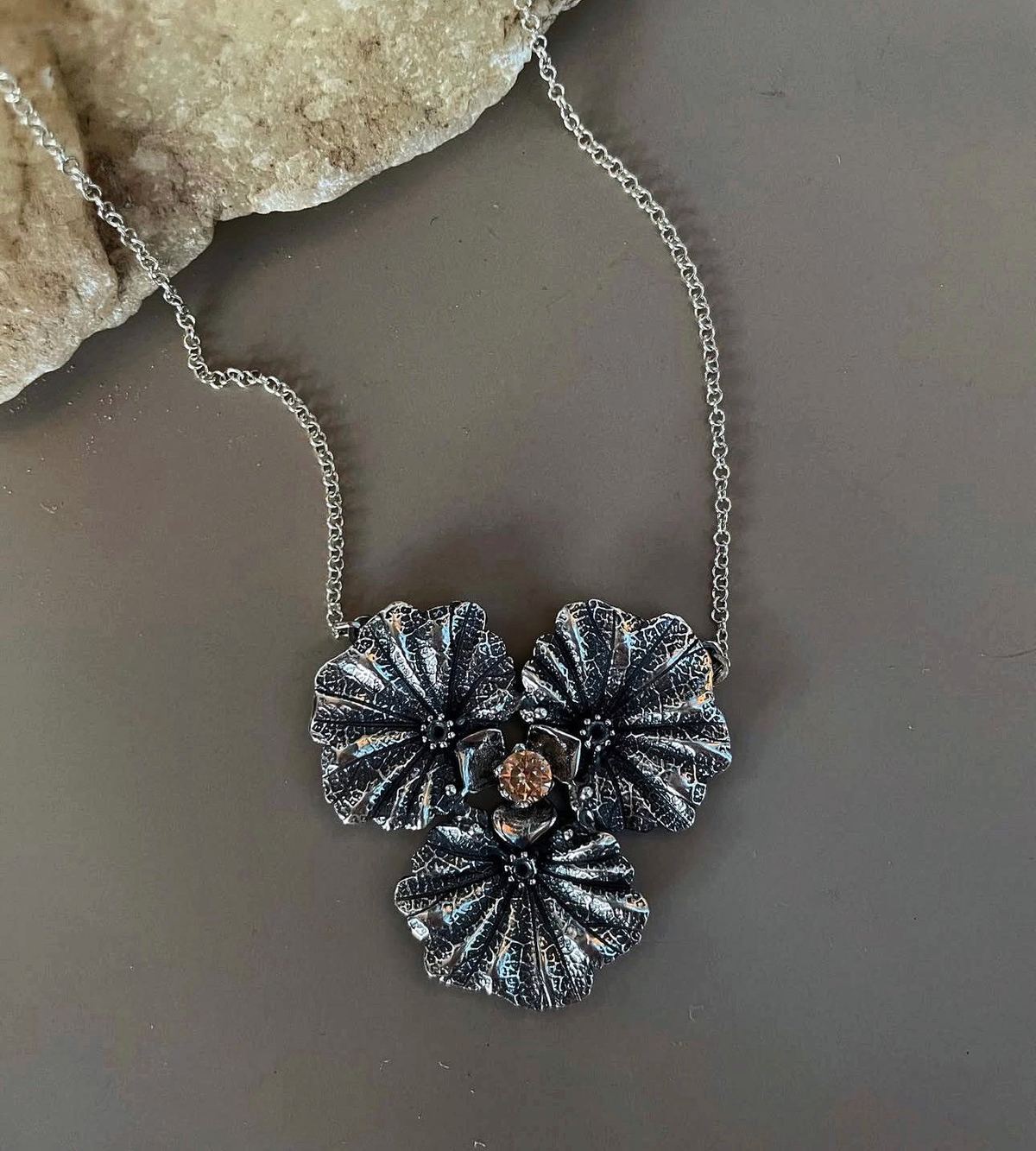 Collar de flor en plata oxidada sobre gris con roca de sal.