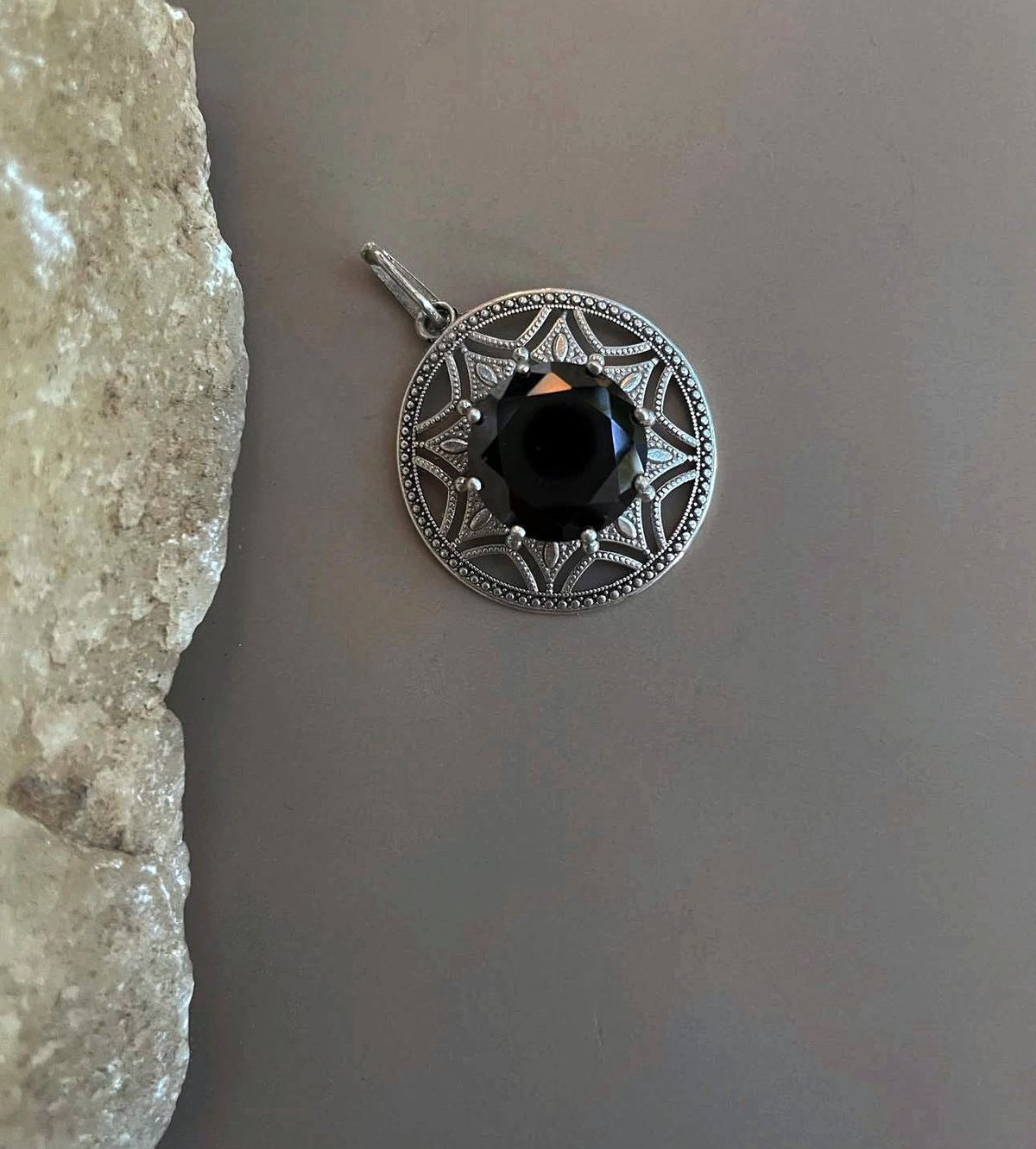 Colgante de plata con ónice en forma de mandala, sobre gris con roca de sal.