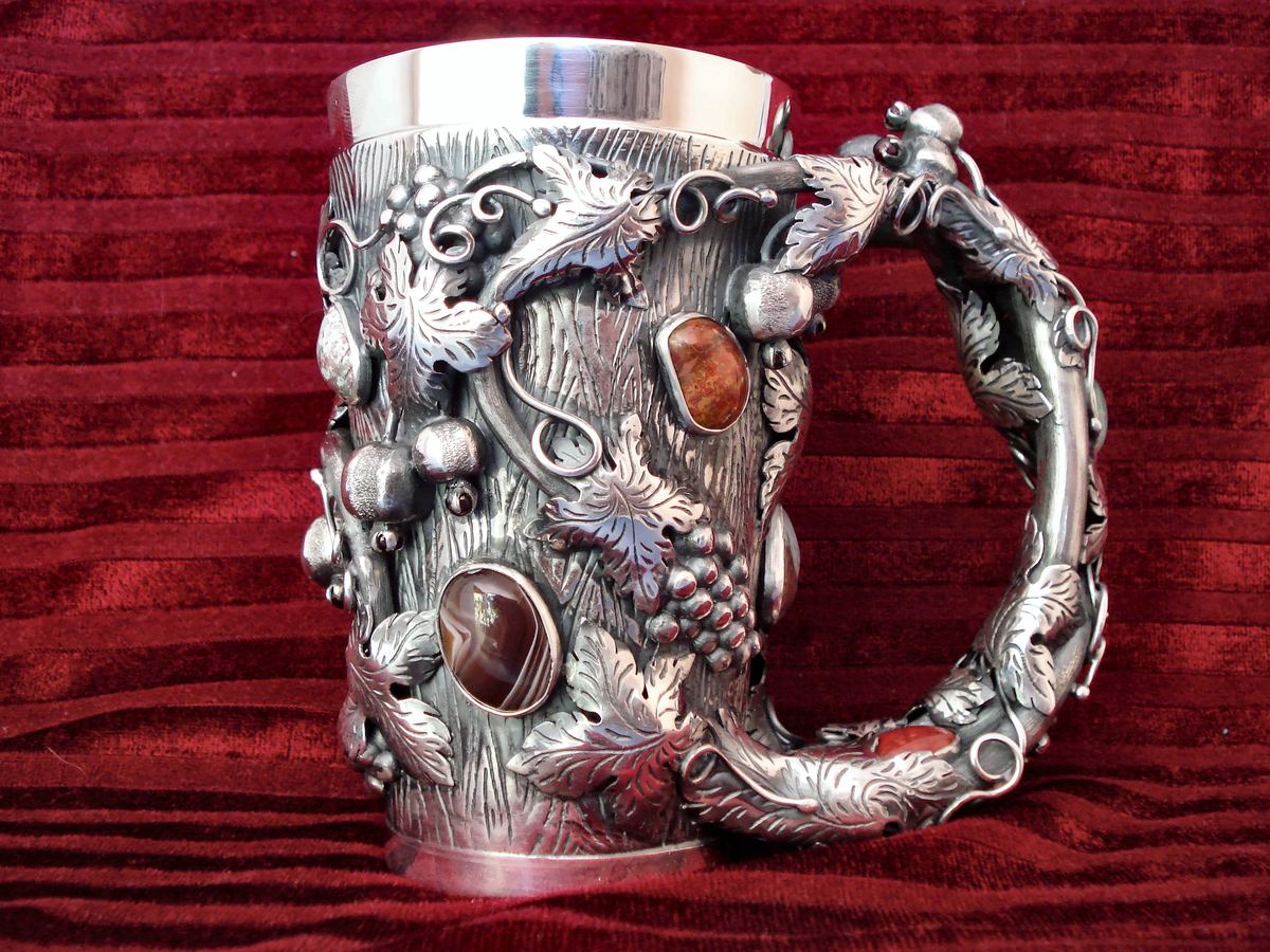 Jarra de plata con relieve de vides y ágatas, sobre terciopelo rojo.