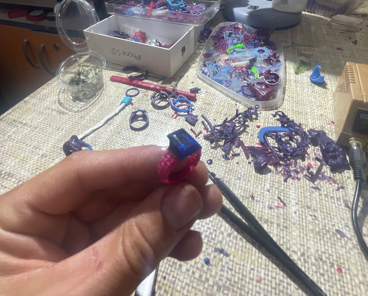Modelo de un anillo tallado en cera, sostenido en la mano sobre el banco de trabajo.